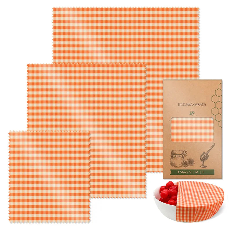 Three orange gingham reusable beeswax food wrap sheets in various sizes for plastic-free kitchen storage.