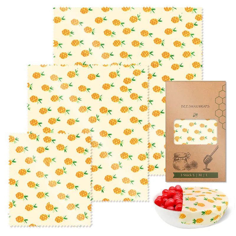 Three reusable beeswax food wraps with pineapple patterns for plastic-free kitchen storage, with packaging and a bowl.