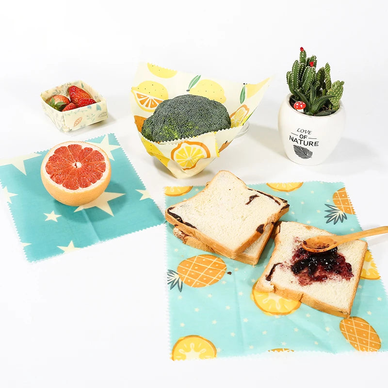 Reusable beeswax food wrap featuring yellow lemon, pineapple, and blue star patterns for plastic-free kitchen storage.