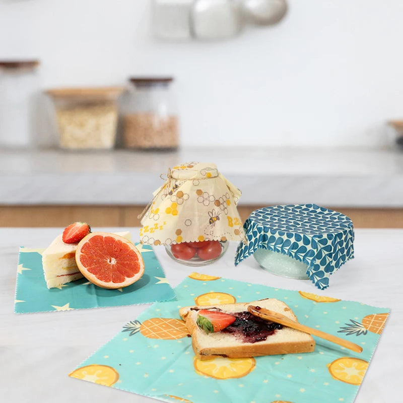 Reusable beeswax food wrap for plastic-free kitchen storage, featuring assorted patterns covering jars and food.