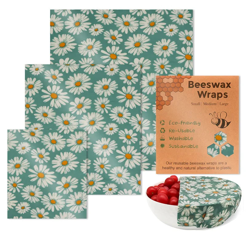 Three square reusable beeswax food wraps featuring a white daisy pattern on teal, with packaging and a bowl covered.