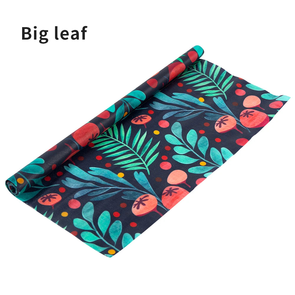 Reusable beeswax food wrap roll in dark blue with teal leaves and red berries pattern for plastic-free kitchen storage.