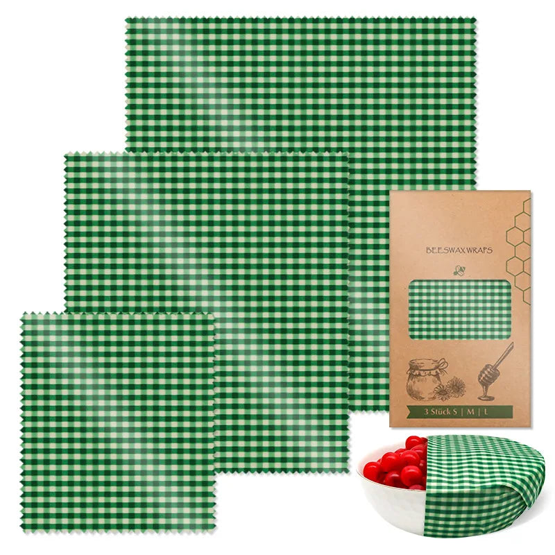 Three green and white checkered reusable beeswax food wraps of varying sizes for plastic-free kitchen storage, with packaging and a bowl.