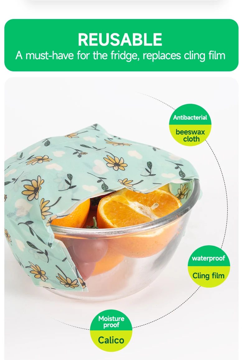 A light blue reusable beeswax food wrap with a floral pattern covers a bowl of fruit for plastic-free kitchen storage.